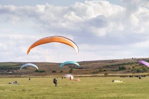 Free photo paragliders silhouette flying over beautiful green landscape under blue sky with clouds.